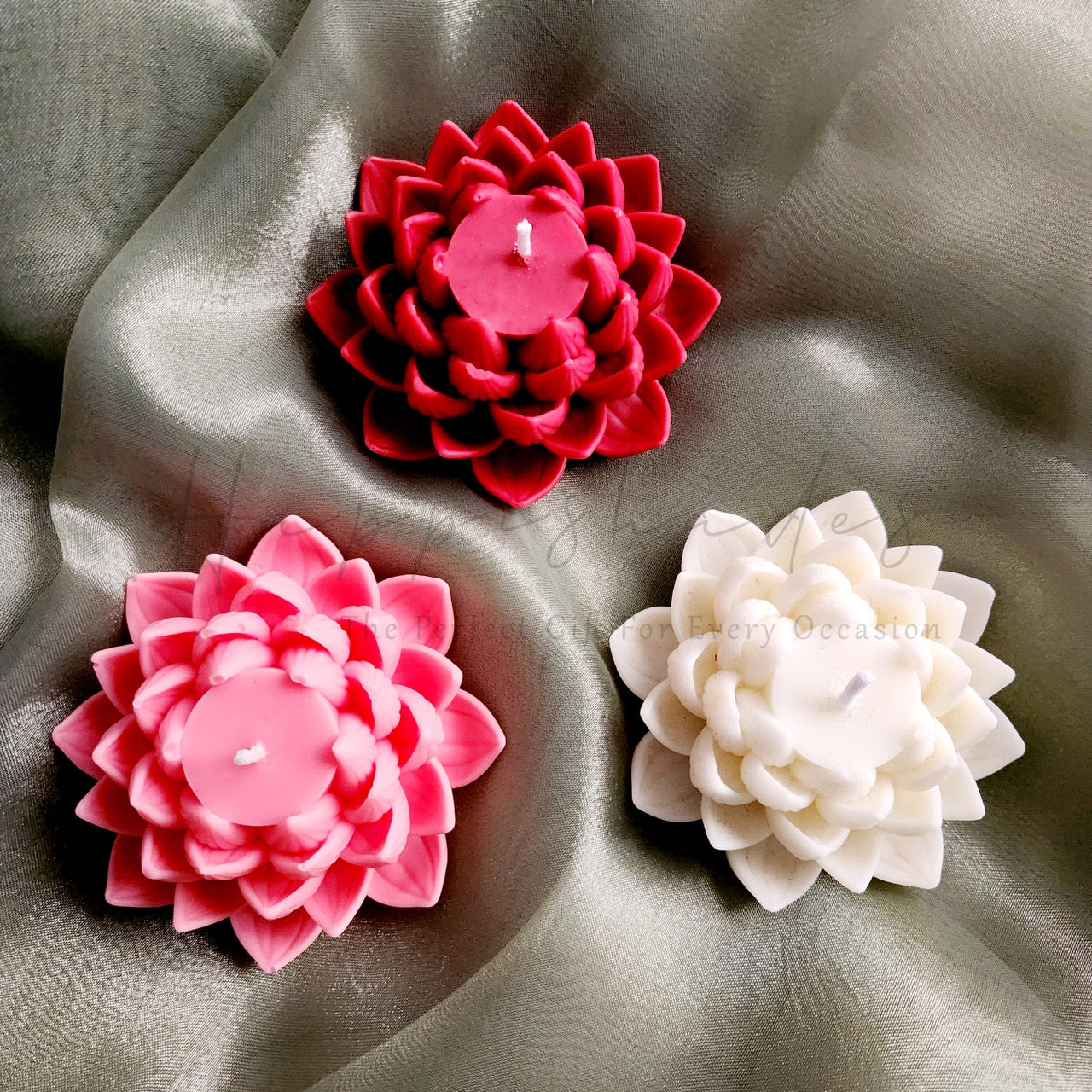 Three flower-shaped candles in red, pink, and white on a textured surface.